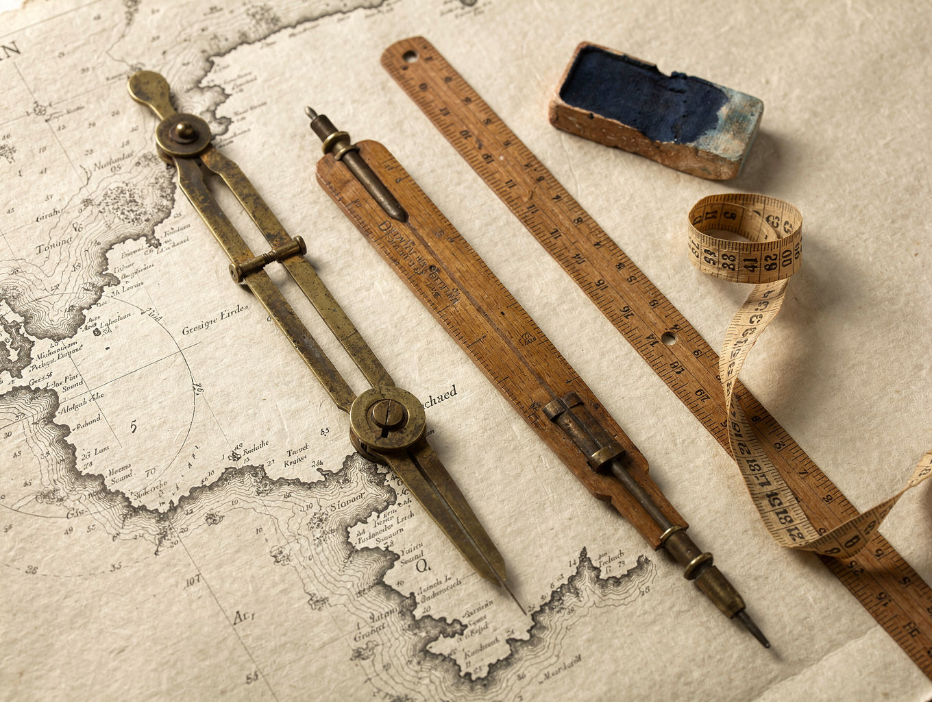 Brass dividers, a wooden parallel rule, linen tape, and Prussian-blue pigment on a cream chart